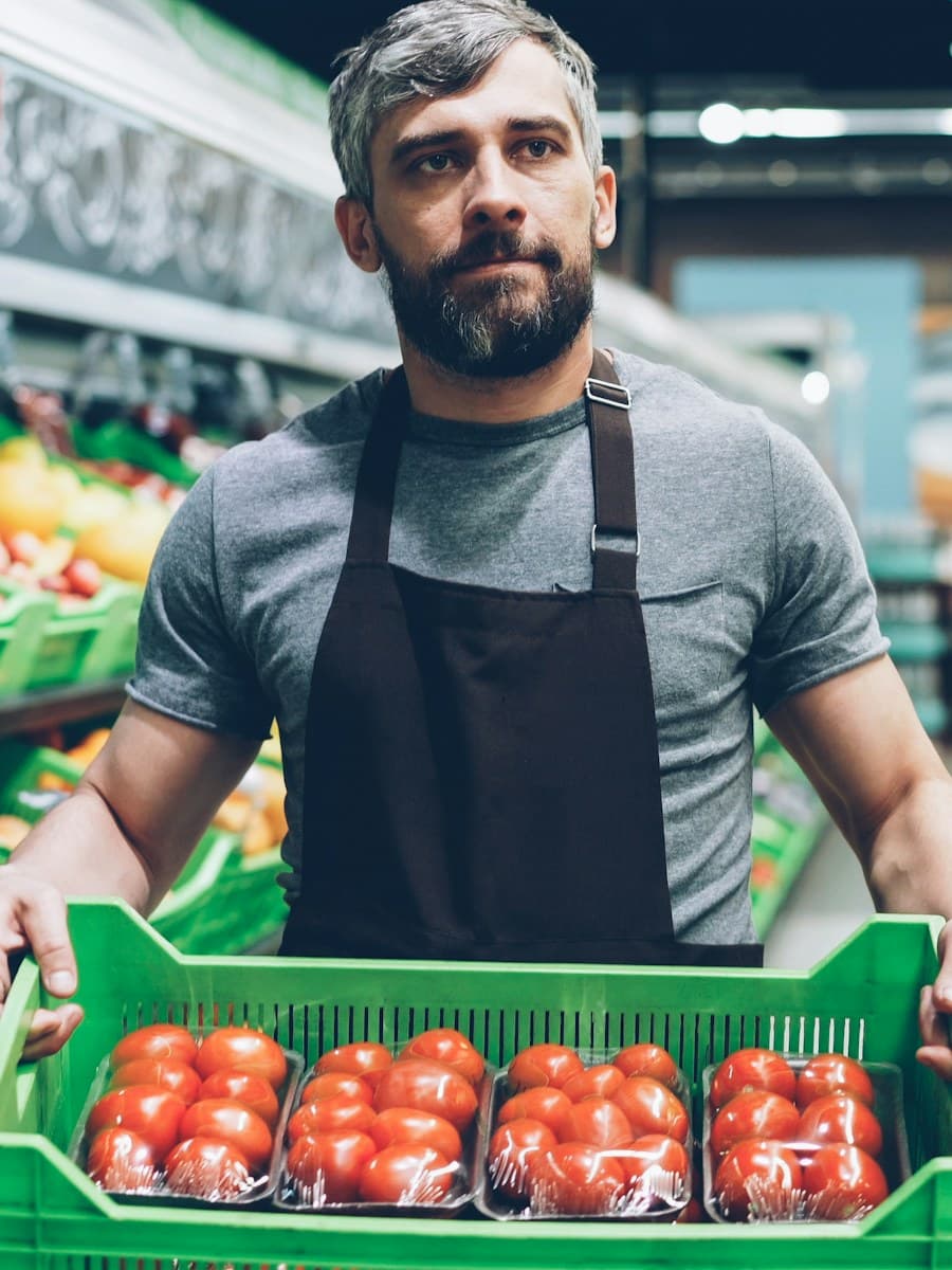 A grocer holding a crate of tomatoes